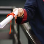 pexels-photo-2292837-2292837 A close-up image of a graduate holding a diploma tied with a red ribbon, symbolizing achievement and success.