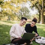 pexels-photo-5553080-5553080 Full length content ethnic male students in casual outfits browsing laptop while sitting on meadow with copybooks and preparing for exam in green park